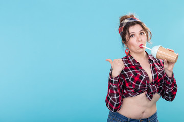 Cute charming young woman in retro clothes is drinking a cocktail from a straw posing against a...
