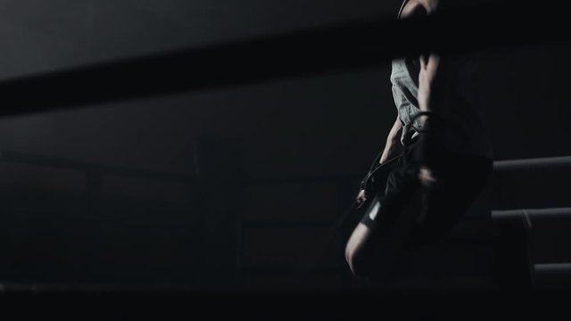 Male boxer wrapped in bandage jumping on the skipping rope in the dark ring. Slow motion. Silhouette. Boxing concept.