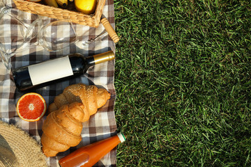 Fototapeta premium Composition with wine, croissants, fruits and towel on grass, top view