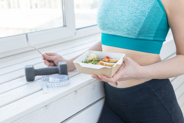 sport, healthy, people concept - Close-up of girl holding salad and dumbbell after fitness training