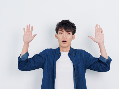 Portrait of a handsome Chinese young man in blue shirt looking at camera with arms open surrender gesture, serious and give up expression, isolated on white background.