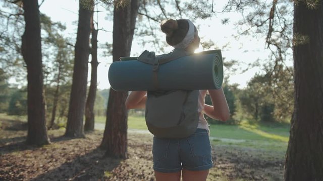 Slow motion shot back woman young tourist with backpack walking in forest sunlight smile look around vacation camping hiking travel wood hike active journey young nature activity close up