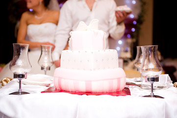 pink and white wedding cake on the background of the bride and groom in defocus