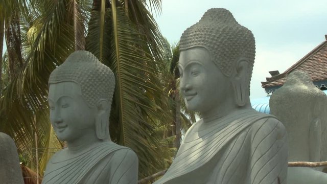 A daylight closeup shot of several large Buddha statues carved from stones in an outdoor setting that can be found in the village of San Tok, Cambodia.