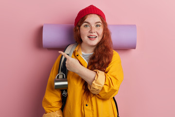 cheerful awesome young woman with freckles pointing with hand and finger to the side looking at the camera.copy space, isolated pink background, advertisement. body language