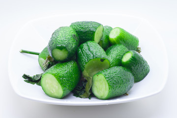 Canned cucumbers on a white plate with leaves and water droplets