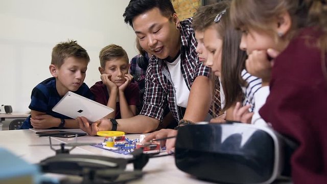 Group of six schoolchildren with teacher using digital tablet when launching fan in an electronic constructor at class