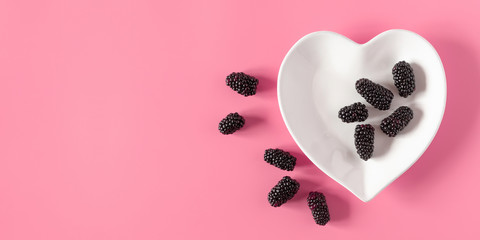 Blackberry pattern. Berry blackberry, white plate in shape heart on pastel pink background. Flat lay, top view, copy space