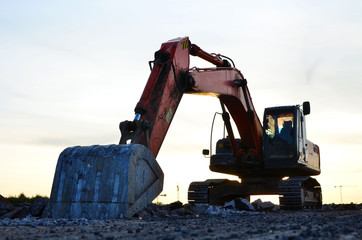 Excavator with a large iron bucket breaks asphalt on a construction site. Demolition work concrete, replacing asphalt, road works. Stone mine in open pit. Loading of stone and rubble - Image