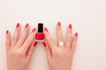 Flat lay groomed woman's hands with red nail varnish bottle isolated on white. Nail varnishing in red color. Manicure concept