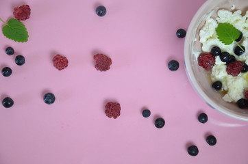 Ricotta with fresh berries and honey on pink table. Cottage cheese, curd cheese or tvorog with berries in bowl. Summer dessert, breakfast or healthy snack. jar of honey blueberries and raspberries