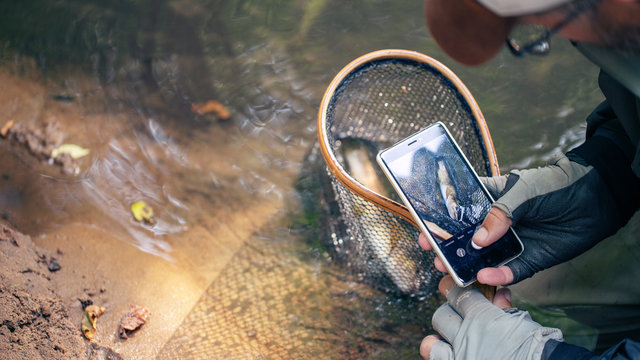 A fisherman photographs his catch on a smartphone.