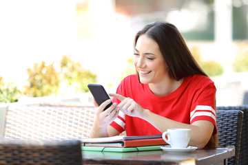 Happy student in red browsing phone content in a bar