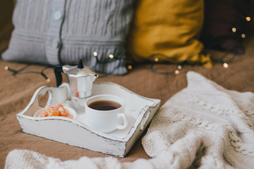 Wooden tray with coffee and kumquat on bed in cozy room.