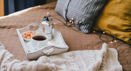 Wooden tray with coffee and kumquat on bed in cozy room.