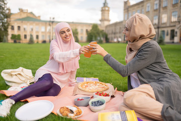 Obraz na płótnie Canvas Cheerful muslim students enjoying pizza time outside