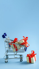 Mini supermarket trolley with gift boxes on blue background.