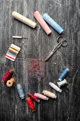 Spools of thread , needles and pins , sewing tools lie on black wooden board