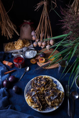 Sweet pasta dessert, noodles with poppy seeds, plum compote from fresh plums, dark background, blue table decorated with fresh flowers. Dry whole poppy plant in background.