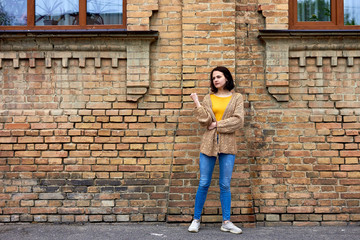 Beautiful young pretty woman in stylish blue jeans nar of old red brick building. Modern european girl enjoying autumn day.