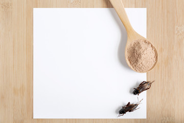 Cricket powder insect for eating as food in wooden spoon with mockup white paper on wood background it is good source of protein edible for future food. Entomophagy concept. Top view. © nicemyphoto