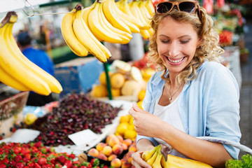 Young woman buying vegetable on stall at the market