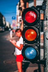 Pedestrian traffic light on the street junction in the city with beautiful bokeh lights, traffic and girl with cell phone in background