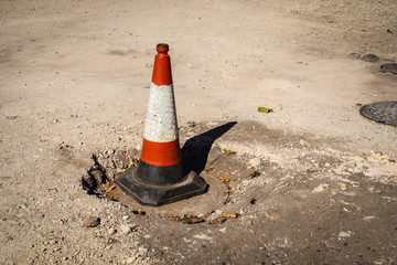 Close up bright orange traffic cone standing on a sewer hatch cover. Road construction works. 