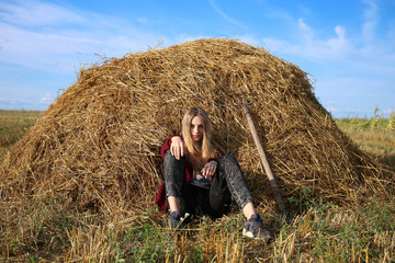 Naklejka na ściany i meble A girl in a rural style is resting sitting on a rye hay in a field.
