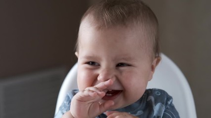 Adorable happy baby boy is looking into the camera. The baby looks around and then smiles and laughs. 1 year old child with brown eyes smiles at home