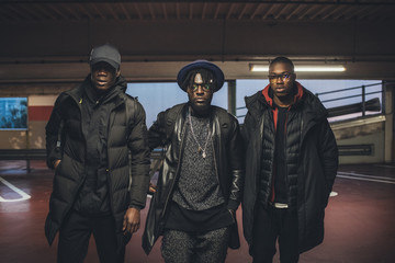 three young black men posing in a parking lot looking away