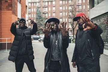 three young men posing outdoor looking camera gesturing with hands