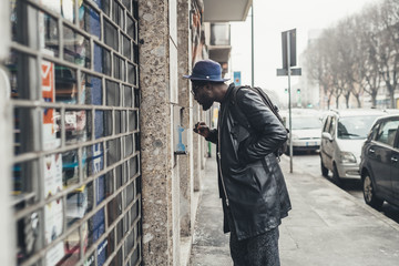 young african man standing in the street searching into mailbox
