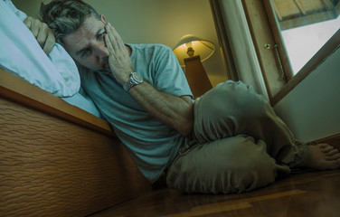 young depressed and desperate man sitting on bedroom floor next to bed suffering depression and anxiety feeling overwhelmed and helpless
