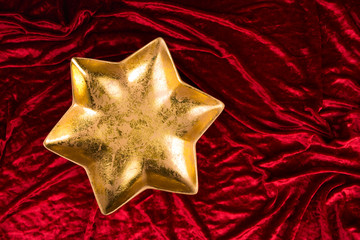 Weihnachtsstern: goldener Teller in Sternform auf rotem Samt