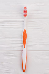 Orange tooth brush on white wooden background. Oral hygiene instrument. Top view, copy space.
