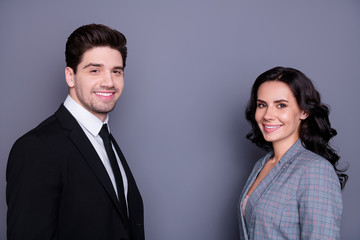 Portrait of beautiful wavy curly brunette haired couple businesspeople looking with toothy smile standing face-to-face wearing black blazer tie jacket isolated over grey background