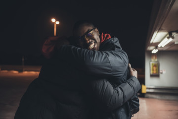 two young men outdoors parking lot greetings hugging