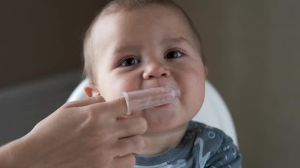 Close-up of mom hands clean the first teeth of her little baby son in the morning. Mother brushing teeth with a silicone fingertip toothbrush. Slow motion