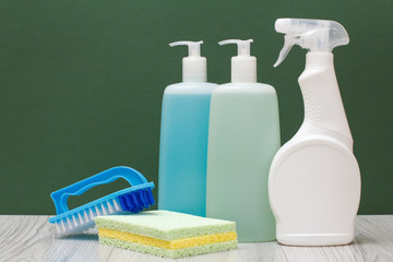 Bottles of dishwashing liquid, glass and tile cleaner, brush and sponges on green background.