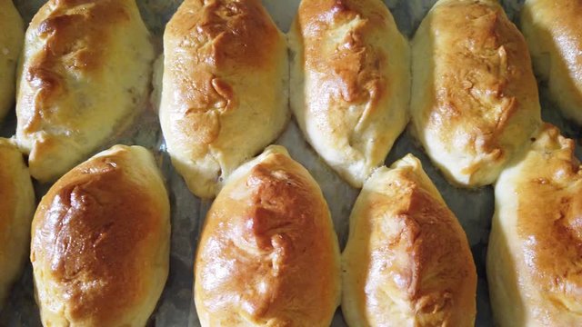 Many traditional delicious baked pasties on tray from oven in bakery. 4K clip with above view