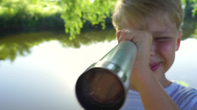 Cute white kid watching through old telescope at something intersting far away in distance. Real time 4k video footage.