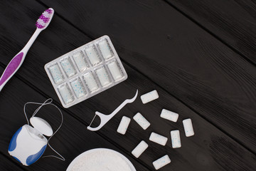 Oral hygiene items on black background. Toothbush, dental floss, chewing gums and tooth powder. Top...