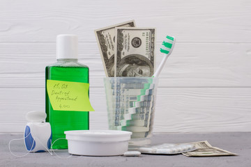 Tools for oral hygiene and dentist appointment reminder. Glass with toothbrush and money, mouthwash...