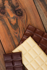 Various chocolate bars on vintage wooden background. White, dark and milk chocolate bars on rustic wood surface. Top view and copy space.