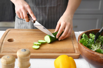 Woman cutting fresh cucumber at table, closeup