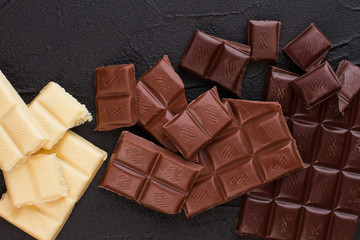 Chocolate bars background. White, milk and dark chocolate pieces on black background close up.