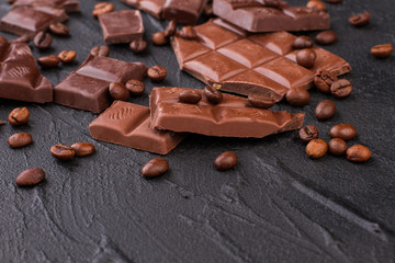 Roasted coffee beans and bars of milk chocolate. Pieces of dark chocolate bar with coffee beans on concrete stone background. Flat lay composition.