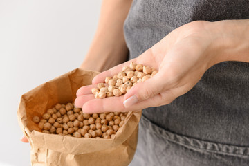 Woman holding bag with raw chickpea on light background, closeup