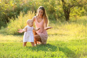 Mother teaching her little baby to walk outdoors